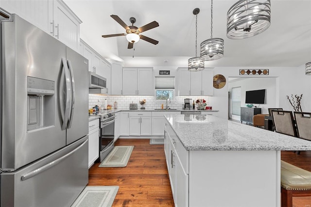 kitchen with appliances with stainless steel finishes, light stone counters, white cabinets, hardwood / wood-style floors, and a center island