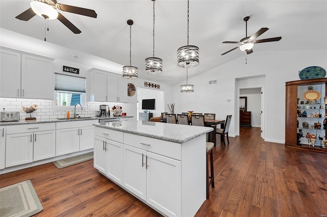 kitchen featuring light stone counters, decorative light fixtures, white cabinetry, and sink