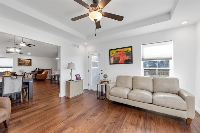 living room featuring dark hardwood / wood-style flooring, a raised ceiling, and ceiling fan