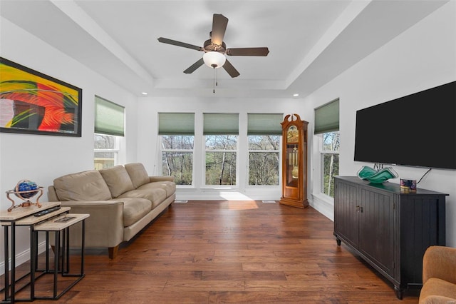 living room featuring dark hardwood / wood-style floors, ceiling fan, and a tray ceiling