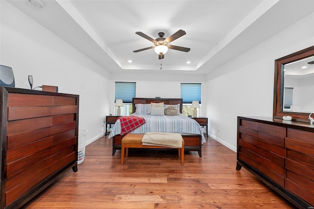 bedroom with a raised ceiling, light hardwood / wood-style flooring, and ceiling fan