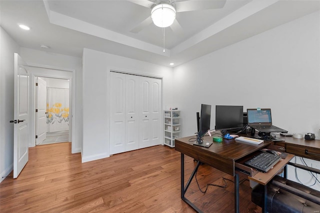 office area featuring light wood-type flooring, a tray ceiling, and ceiling fan