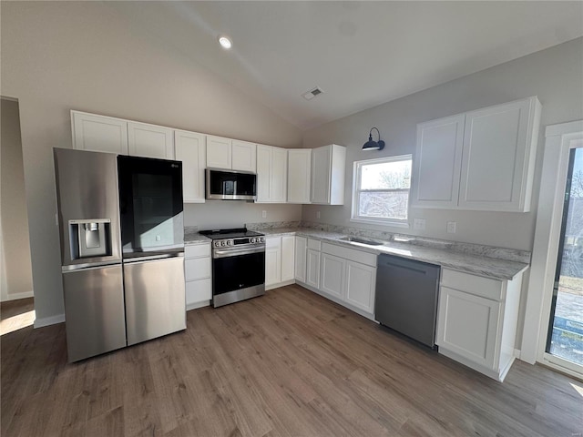 kitchen with visible vents, wood finished floors, white cabinets, stainless steel appliances, and a sink