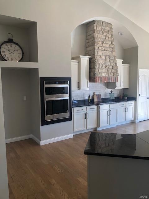 kitchen featuring lofted ceiling, dark wood-type flooring, white cabinets, decorative backsplash, and double oven