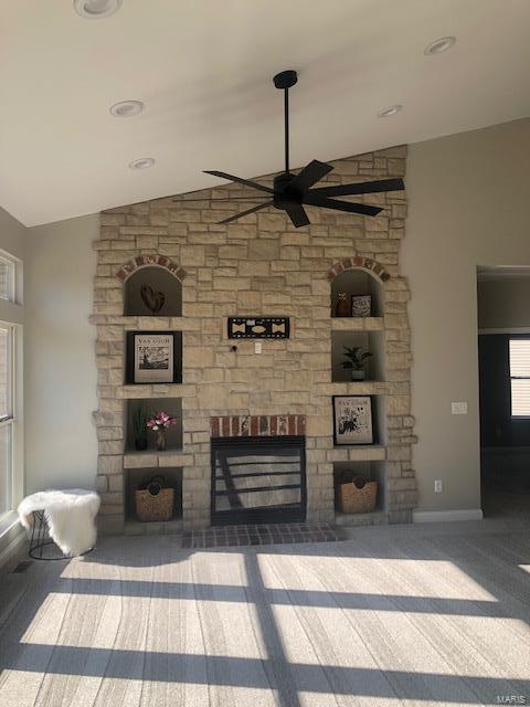 unfurnished living room with carpet flooring, ceiling fan, a stone fireplace, built in features, and lofted ceiling