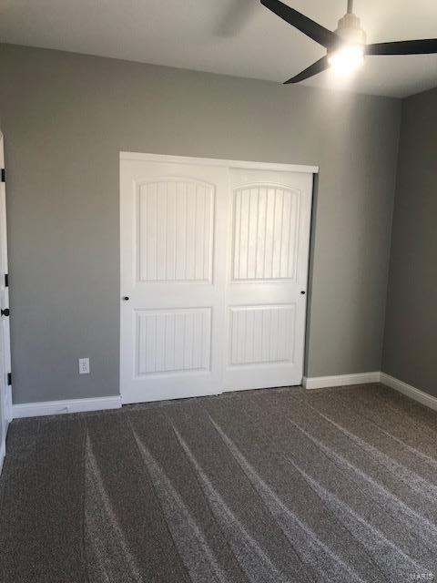 unfurnished bedroom featuring dark colored carpet, ceiling fan, and a closet