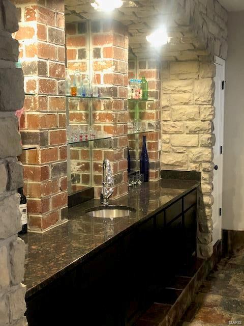 bar with sink, dark stone counters, and brick wall