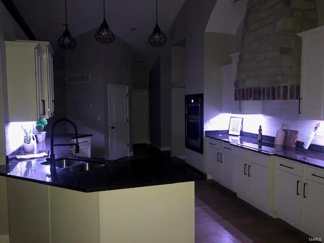 kitchen with sink, high vaulted ceiling, double oven, decorative light fixtures, and white cabinets