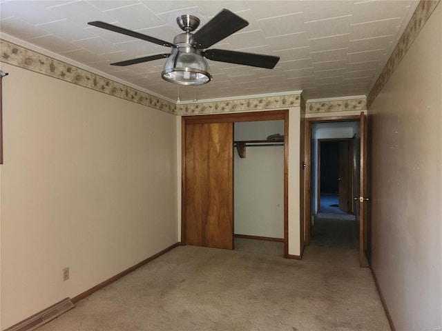 unfurnished bedroom with ornamental molding, a closet, ceiling fan, and light colored carpet