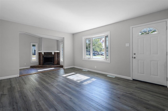 unfurnished living room with a healthy amount of sunlight, dark wood-type flooring, and a brick fireplace