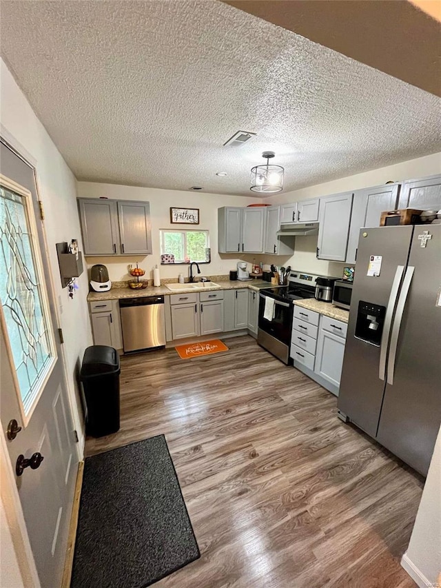 kitchen with a textured ceiling, stainless steel appliances, sink, hardwood / wood-style flooring, and gray cabinets