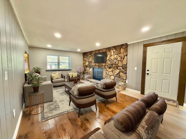 living room with a stone fireplace, light wood-type flooring, and wooden walls