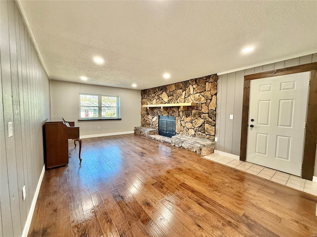 unfurnished living room with a textured ceiling, wood walls, wood-type flooring, and a fireplace