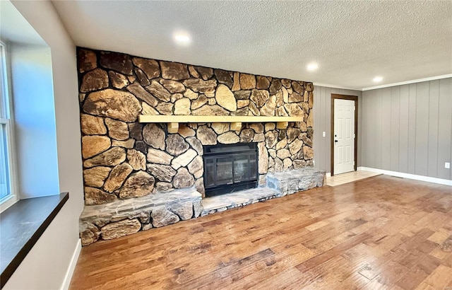 unfurnished living room featuring hardwood / wood-style floors, a stone fireplace, a textured ceiling, and wooden walls