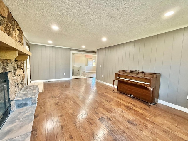 miscellaneous room featuring a stone fireplace, wood walls, a textured ceiling, and light wood-type flooring