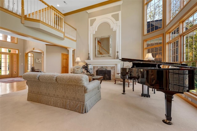 carpeted living room featuring a high ceiling, a tiled fireplace, decorative columns, and ornamental molding