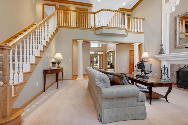 carpeted living room featuring a high ceiling, a tiled fireplace, crown molding, and ornate columns