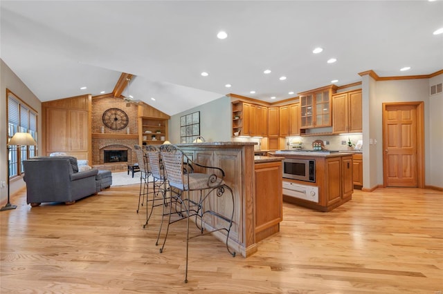 kitchen featuring a fireplace, a kitchen bar, light hardwood / wood-style flooring, a kitchen island, and stainless steel microwave