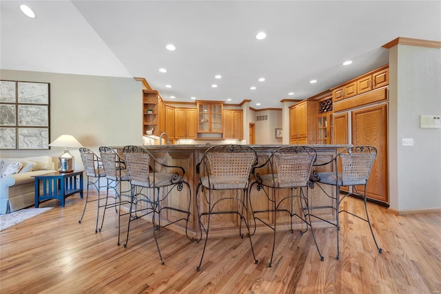 kitchen with kitchen peninsula, light wood-type flooring, paneled built in fridge, and a breakfast bar