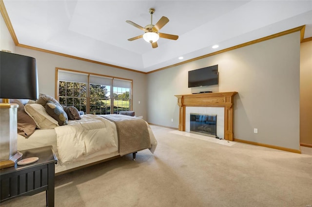 carpeted bedroom featuring a tile fireplace, ceiling fan, and a tray ceiling