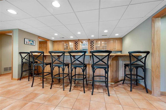 bar with light tile patterned floors and a paneled ceiling