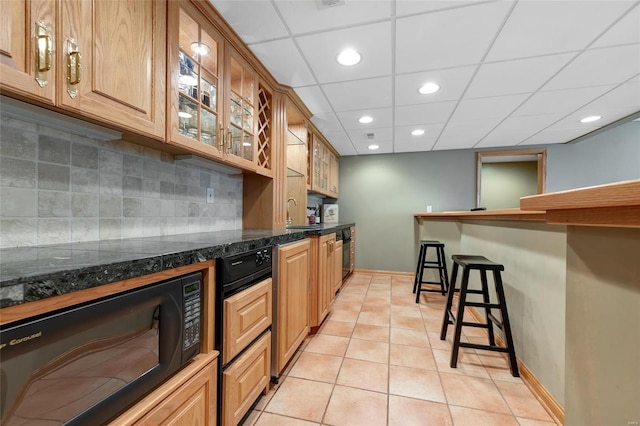 kitchen featuring a paneled ceiling, light tile patterned floors, a kitchen bar, sink, and tasteful backsplash