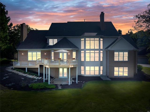 back house at dusk with a yard, a wooden deck, and a patio