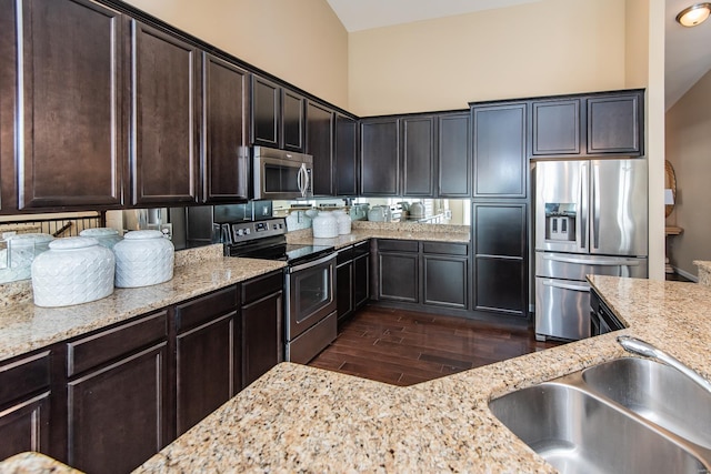 kitchen featuring light stone countertops, appliances with stainless steel finishes, dark brown cabinetry, vaulted ceiling, and dark hardwood / wood-style floors