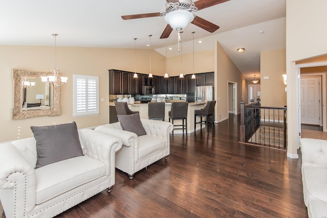 living room featuring ceiling fan with notable chandelier, dark wood-type flooring, and high vaulted ceiling