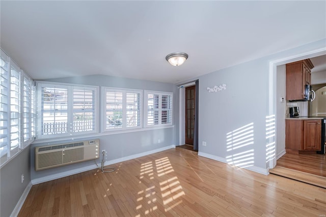 interior space featuring vaulted ceiling, a healthy amount of sunlight, an AC wall unit, and light hardwood / wood-style flooring