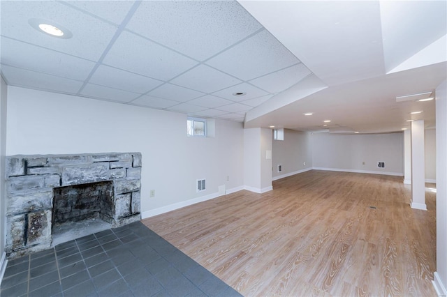 basement with a paneled ceiling, a stone fireplace, and wood-type flooring