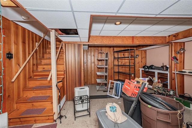 basement featuring a drop ceiling and wood walls