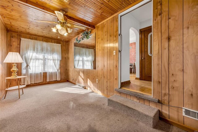 carpeted empty room with ceiling fan, wooden walls, and wood ceiling