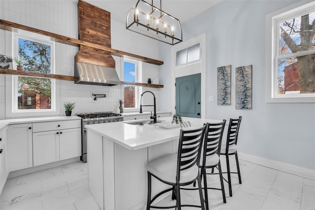 kitchen featuring hanging light fixtures, sink, stainless steel stove, an island with sink, and white cabinetry