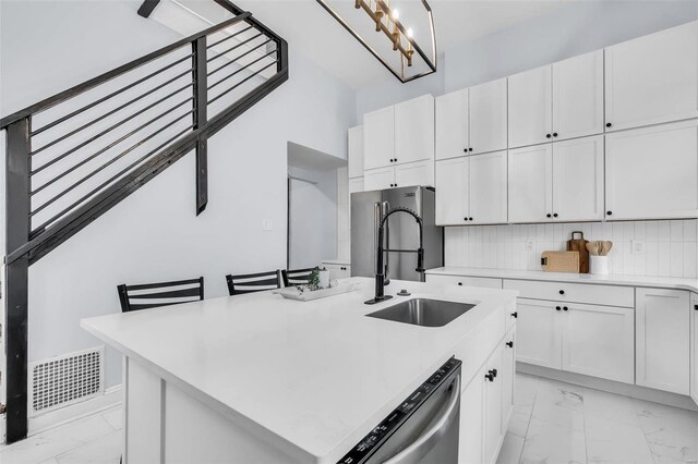 kitchen with tasteful backsplash, stainless steel appliances, a kitchen island with sink, sink, and white cabinets