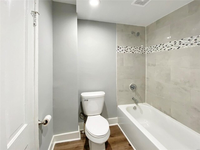 bathroom with hardwood / wood-style flooring, tiled shower / bath combo, and toilet