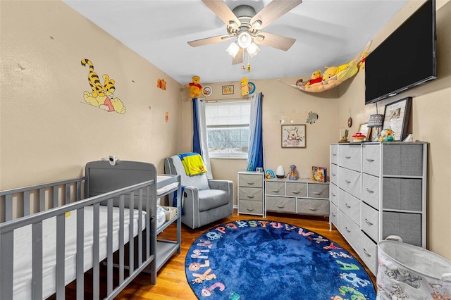 bedroom featuring ceiling fan, a crib, and light wood-type flooring