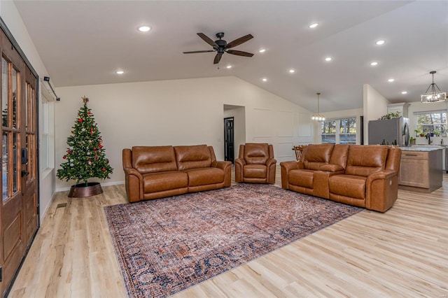 living room with ceiling fan with notable chandelier, light hardwood / wood-style flooring, and lofted ceiling