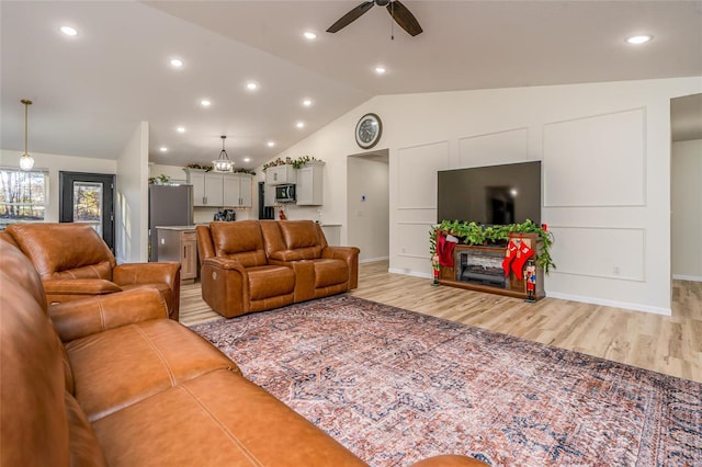 living room featuring ceiling fan, lofted ceiling, and light hardwood / wood-style flooring