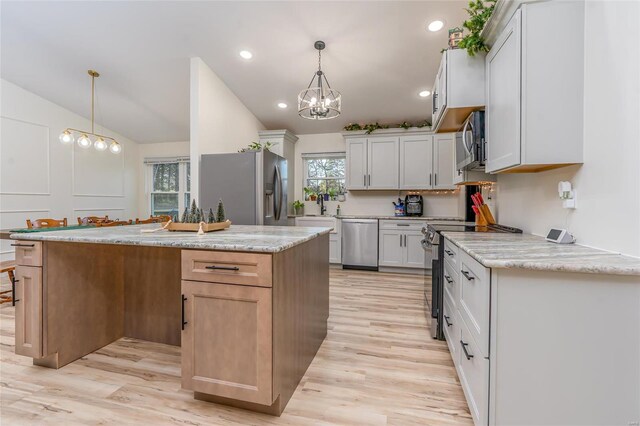 kitchen featuring white cabinets, vaulted ceiling, appliances with stainless steel finishes, decorative light fixtures, and a kitchen island