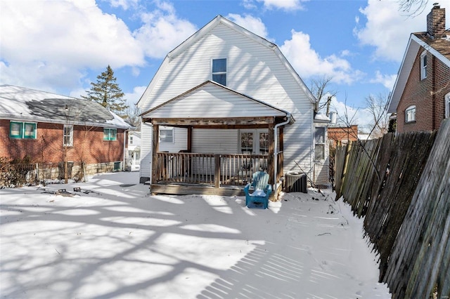 snow covered back of property featuring fence and a gambrel roof