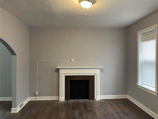 unfurnished living room with dark hardwood / wood-style flooring and a brick fireplace