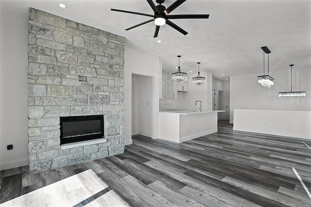 unfurnished living room featuring ceiling fan with notable chandelier, a stone fireplace, dark hardwood / wood-style flooring, and sink