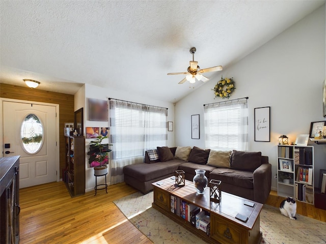 living room with ceiling fan, light wood-type flooring, a textured ceiling, and vaulted ceiling