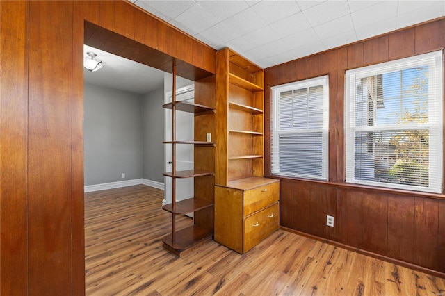 interior space featuring built in shelves, wood walls, and light hardwood / wood-style flooring