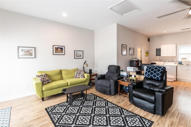 living room with washer and clothes dryer, electric panel, sink, ceiling fan, and light wood-type flooring