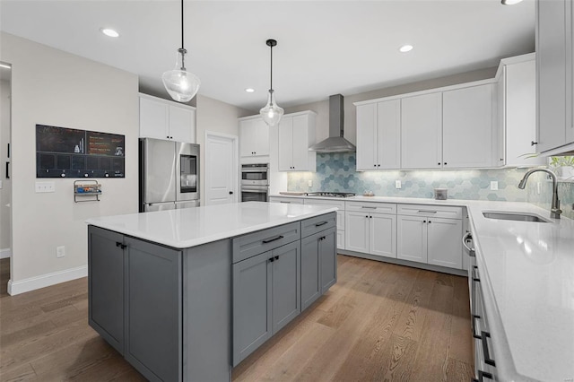 kitchen with a center island, sink, gray cabinets, appliances with stainless steel finishes, and wall chimney exhaust hood