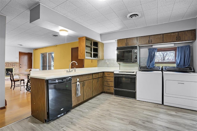 kitchen featuring washing machine and dryer, kitchen peninsula, black appliances, and light wood-type flooring