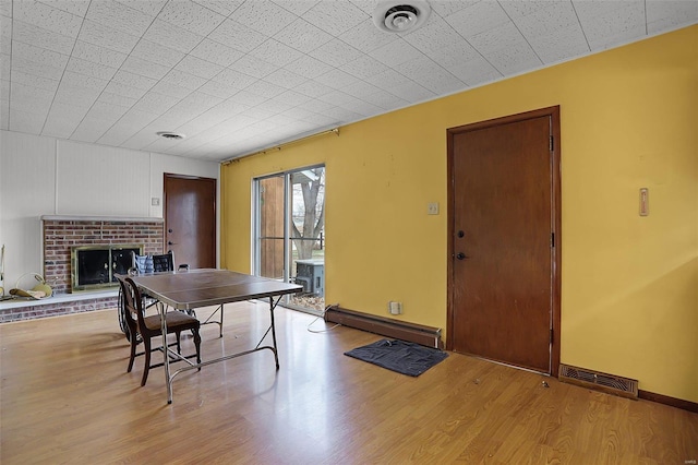 dining area with light wood-type flooring, baseboard heating, and a brick fireplace