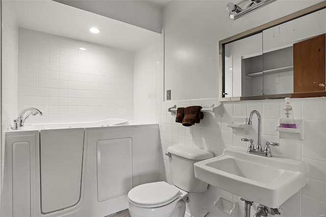 bathroom featuring a bathtub, toilet, sink, and tile walls